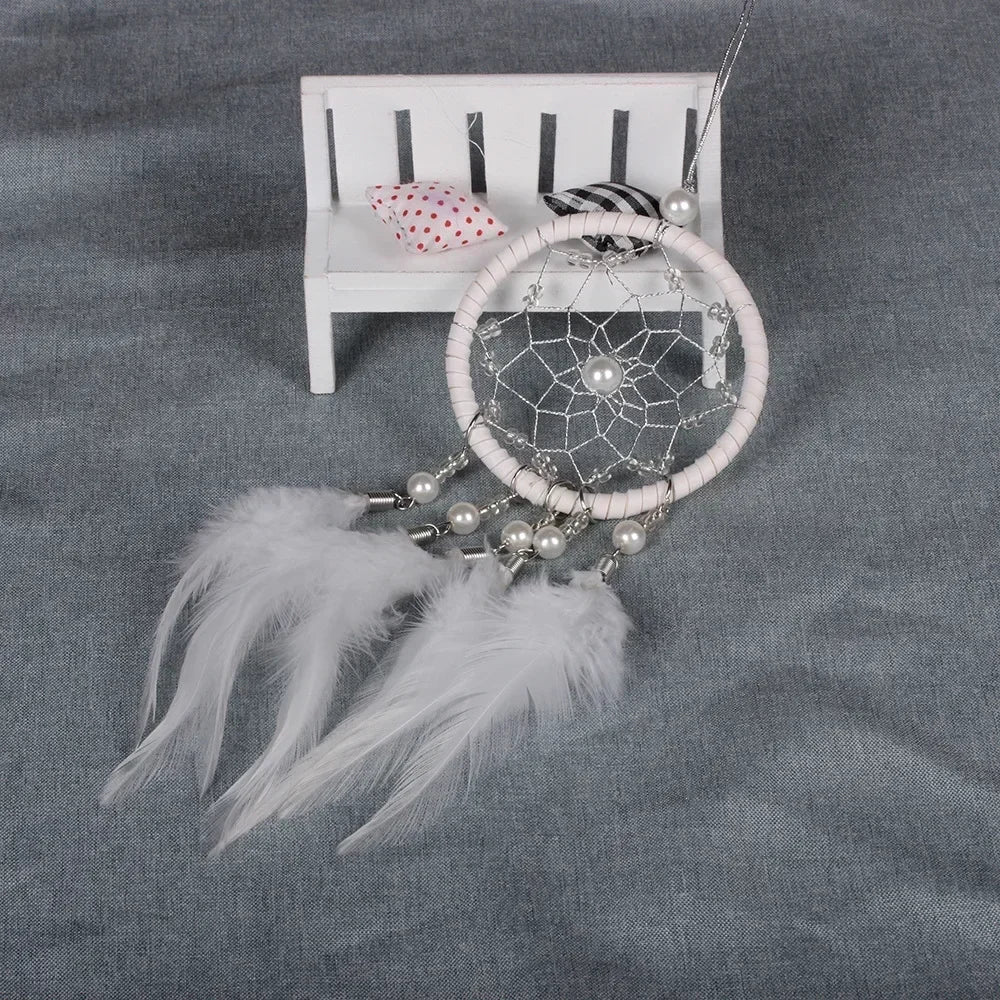 A dream catcher pendant featuring a crystal mirror, beads, and white feathers displayed on a white wooden rack.