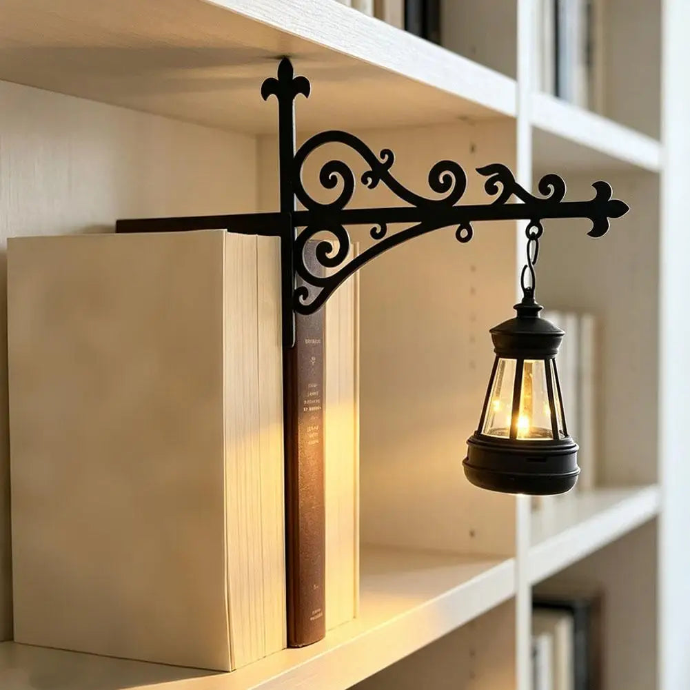 A black wrought iron book stand holds a vintage-style lantern with a soft warm glow on a white shelf.