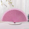 A pink wooden hand fan with white polka dots is displayed on a white surface.
