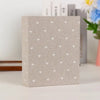 Quadratisches Leinen-Coverfotoalbum mit hellem beige Hintergrund und kleinen weißen Herzmustern, neben Büchern.