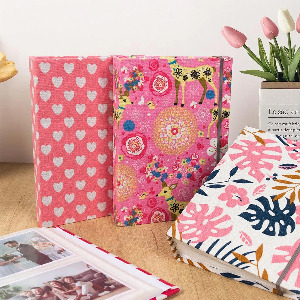 A set of pink and floral linen printed photo albums with decorative covers and a potted plant.