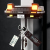 A classic car headlight key holder with LED illumination mounted on a wall, featuring a dark brown casing and brass key.