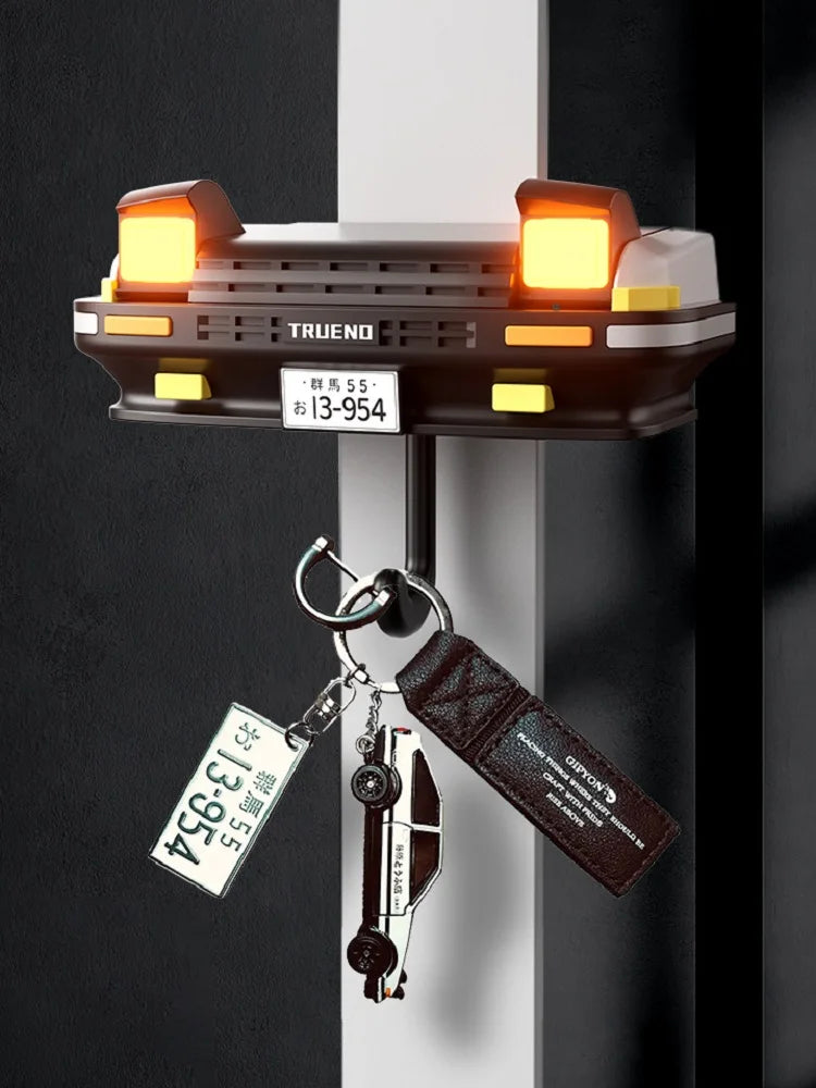A classic car headlight key holder with LED illumination mounted on a wall, featuring a dark brown casing and brass key.