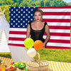 A woman in a black top stands in front of an American flag banner with yellow and orange balloons on a checkered blanket.