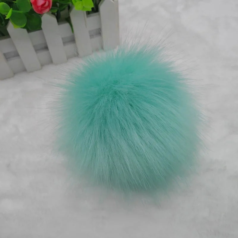 Pompon en fausse fourrure bleu sarcelle posé sur une surface blanche à côté d'un pot en bois.
