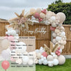 A balloon garland arch kit featuring pink and beige balloons arranged outdoors against a wooden fence.