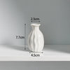 A white ceramic mini vase with a textured surface is shown on a shelf.