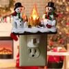 A decoration featuring two snowmen with a campfire light on top, mounted on a wall outlet.