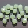 A collection of square cut glass crystal beads in a pale green color arranged on a dark surface.