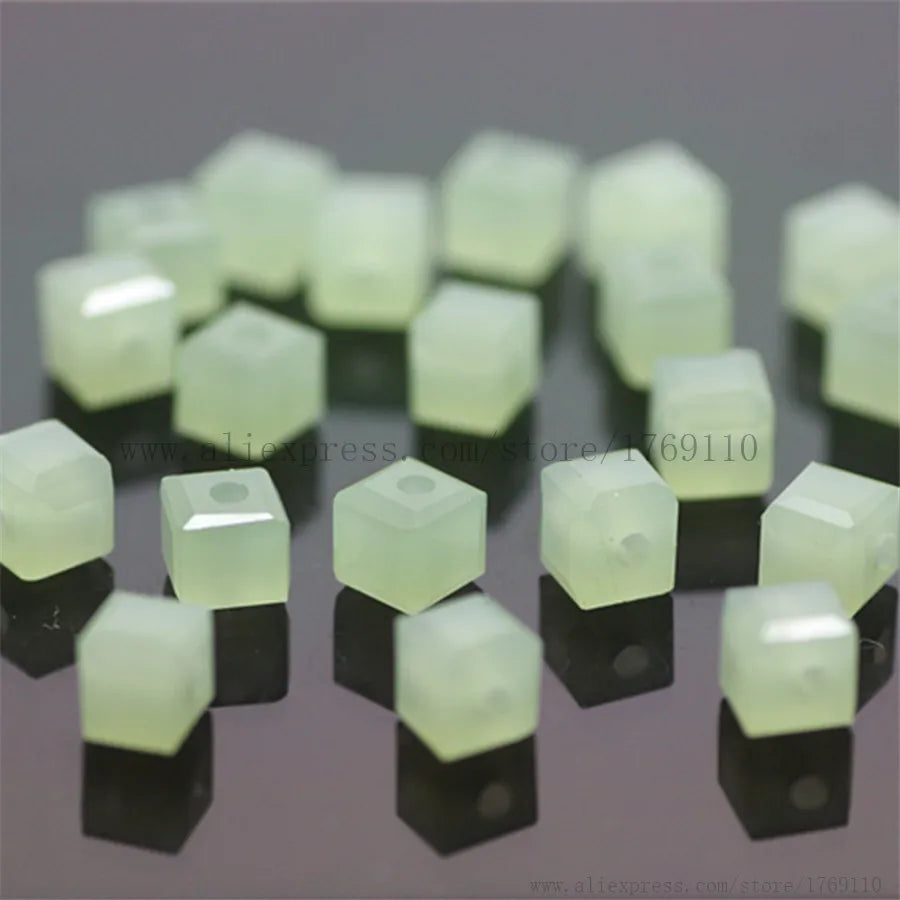 A collection of square cut glass crystal beads in a pale green color arranged on a dark surface.