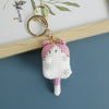 A handcrafted crochet cat keychain pendant with pink and white yarn, attached to a gold-colored metal ring.