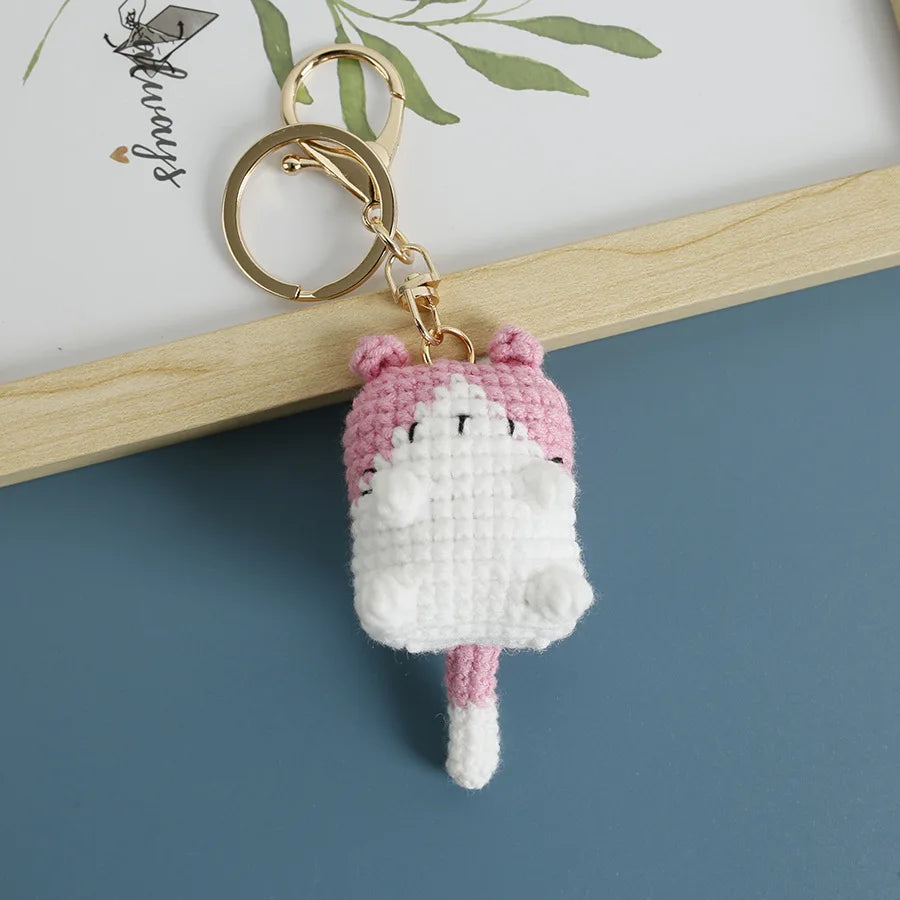 A handcrafted crochet cat keychain pendant with pink and white yarn, attached to a gold-colored metal ring.