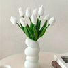 A bouquet of six white artificial tulips in a white vase on a light surface.
