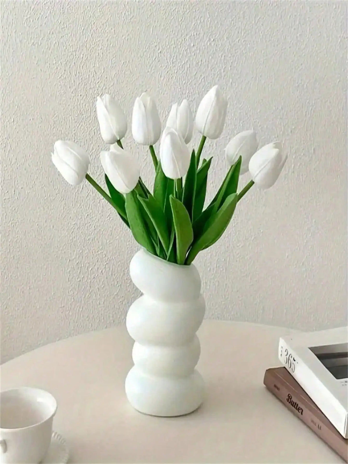 A bouquet of six white artificial tulips in a white vase on a light surface.