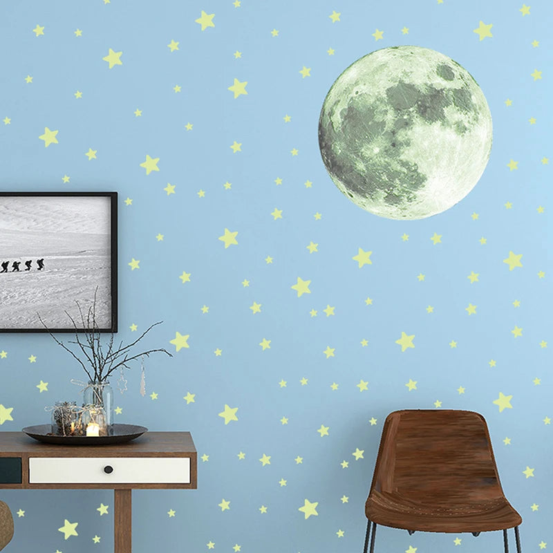 A light blue wall decorated with yellow stars and a large pale green moon, next to a framed photo and a wooden chair.