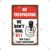 A vintage metal warning sign with a distressed red background and white text stating No Trespassing and We Don't Dial 911 We 
