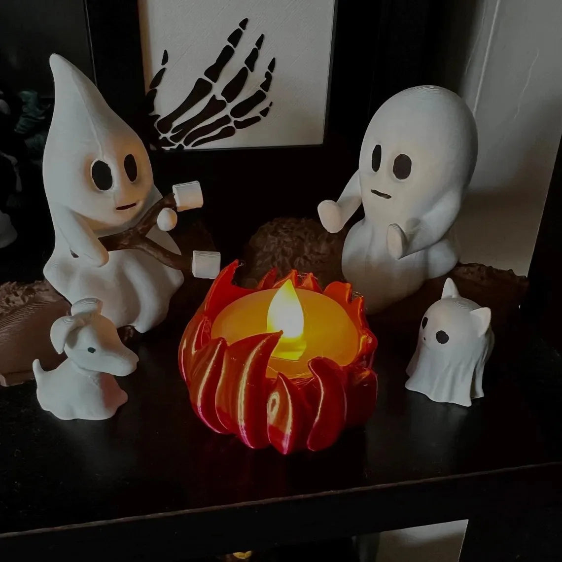 A set of white ghost figures and a red candle in a flame setting for Halloween decor.
