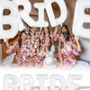 A group of women posing with large white letter foil balloons spelling the word BRIDE