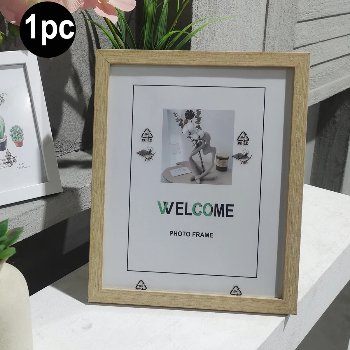A wooden photo frame with a light wood border displaying the word WELCOME and a floral arrangement.