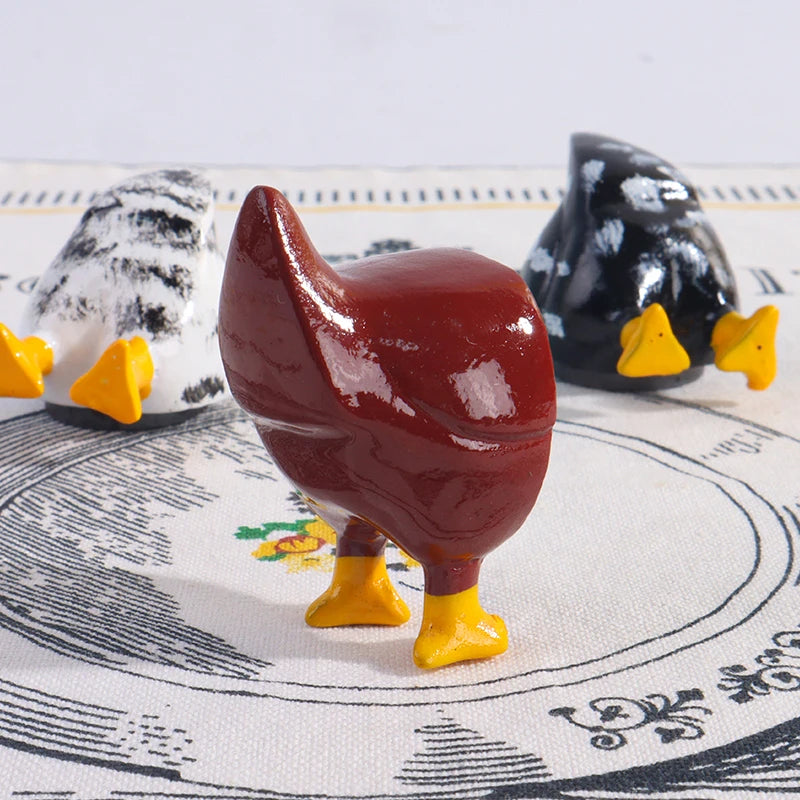 A set of three playful chicken butt fridge magnets in white, red, and black against a patterned cloth.