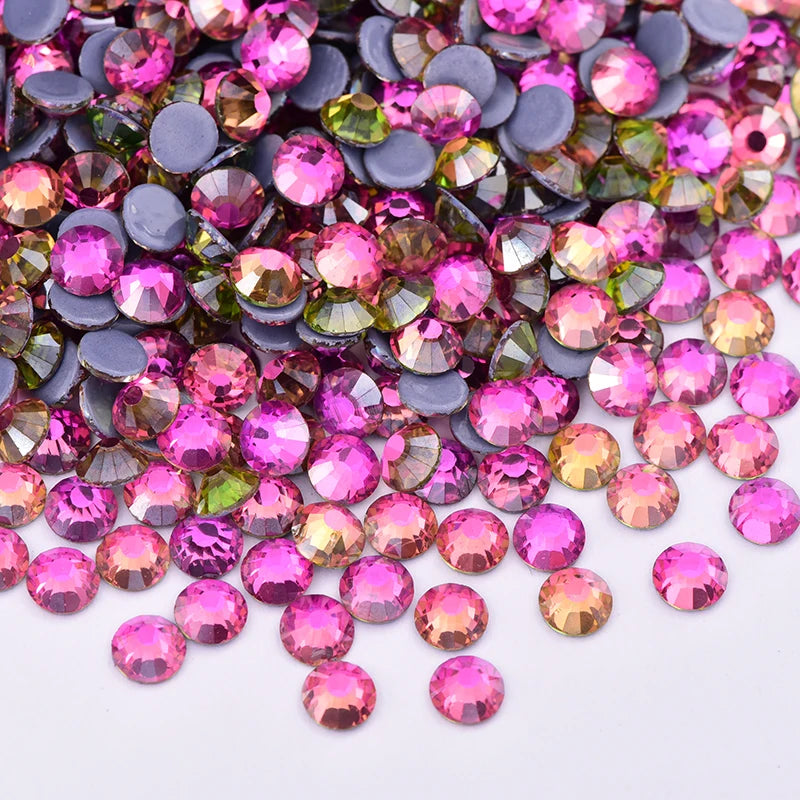 A close-up view of mixed colored glass rhinestones and crystals in various sizes scattered on a white surface.