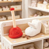 A plush toy resembling a toilet paper poop plunger with a red base and a beige handle is displayed on a wooden shelf.