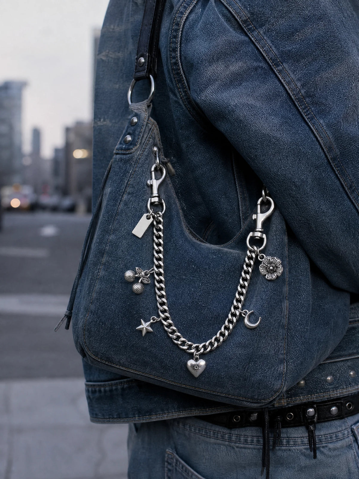Gros plan d'une veste en denim foncé avec un charm de sac en chaîne argentée suspendu à la sangle.