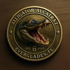A round gold-colored collectible coin featuring a detailed illustration of an alligator head with an open mouth.
