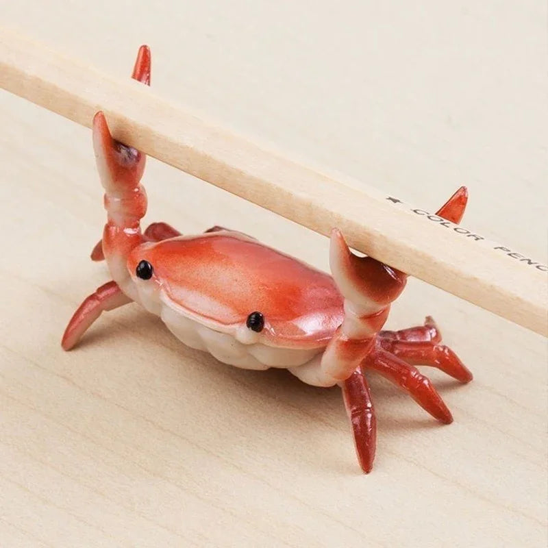 A small, crab-shaped desk organizer made of resin, featuring a pen and phone holder, resting on a wooden surface.