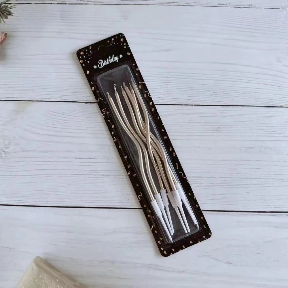 A package of elegant spiral birthday candles in a dark box with a clear insert on a white wooden surface.