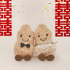 Two fluffy beige plush toys resembling peanuts with black bowties and reindeer antlers against a red geometric background