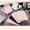 A collection of pink, white, and black portable folding HD makeup mirrors displayed on a glass surface.