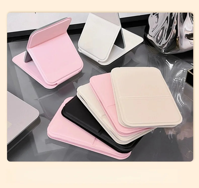 A collection of pink, white, and black portable folding HD makeup mirrors displayed on a glass surface.