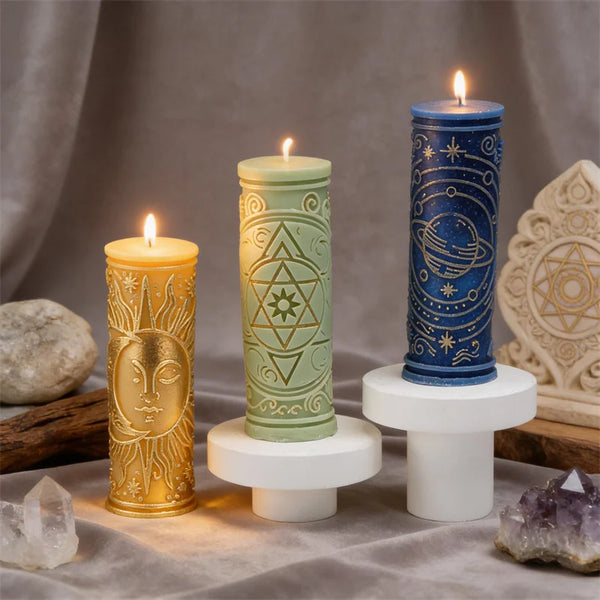 Three pillar candles in gold, green, and blue with celestial symbols displayed on a cloth.