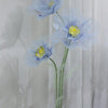 A large artificial silk blue poppy flower displayed on a green stand against a white curtain backdrop.