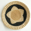 Round woven straw wall decor hanging with a black geometric pattern on a natural straw background