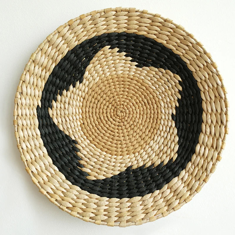 Round woven straw wall decor hanging with a black geometric pattern on a natural straw background