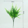 Artificial fern and leaf sprigs in green displayed in a glass vase.