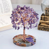 A crystal money tree decor featuring purple amethyst-like crystals on a wooden branch mounted on a polished stone base.