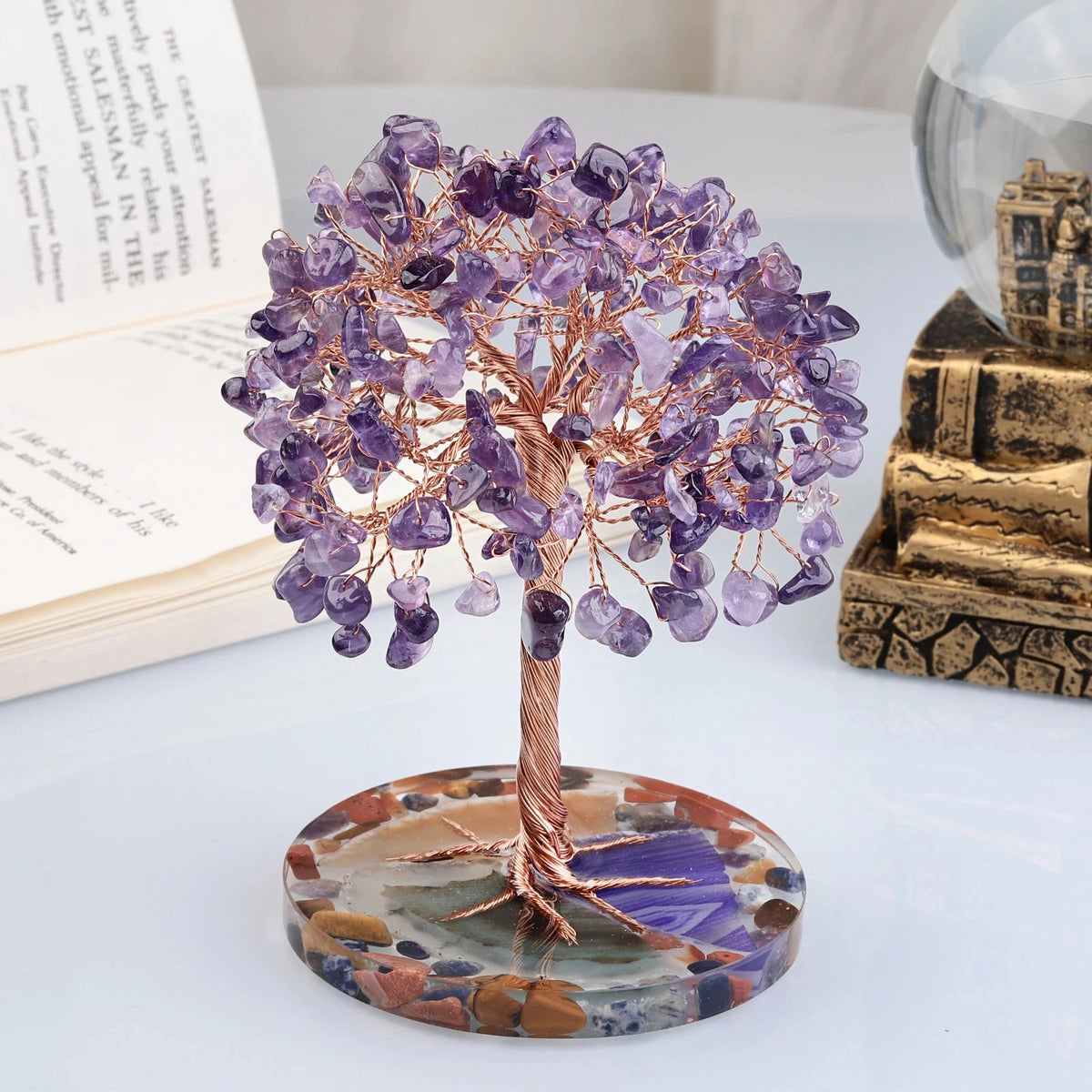 A crystal money tree decor featuring purple amethyst-like crystals on a wooden branch mounted on a polished stone base.