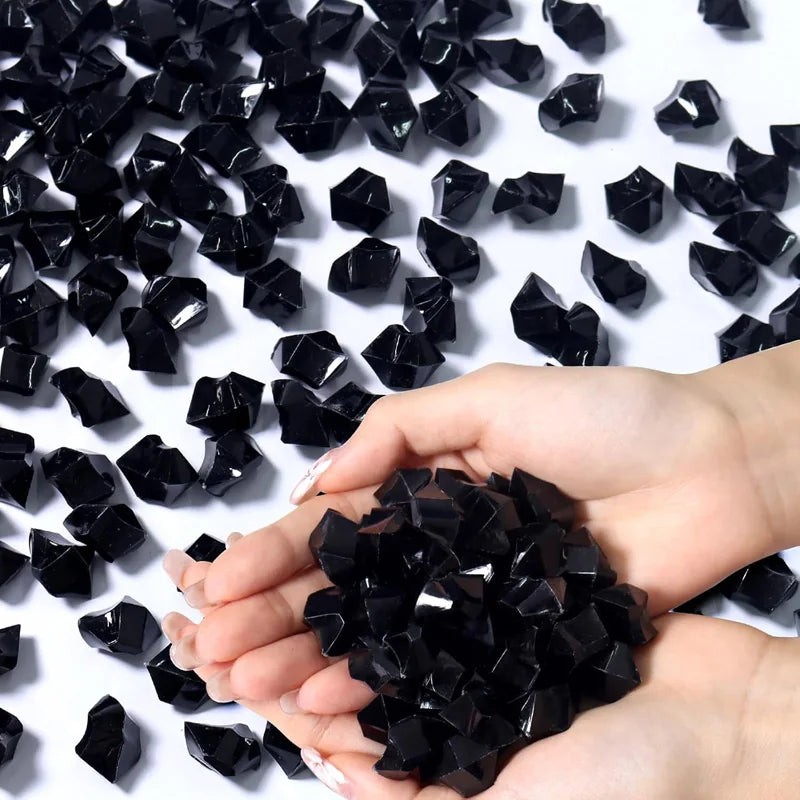 A hand is holding a pile of black decorative crushed diamond acrylic pebbles.