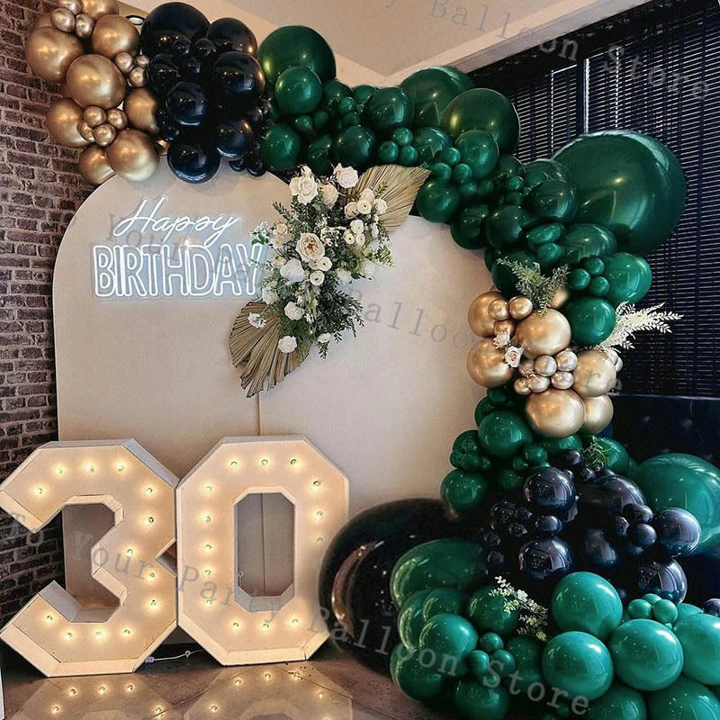 A balloon garland featuring green, gold, and black balloons decorating a birthday backdrop.