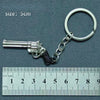 A silver alloy gun model miniature keyring with a realistic grip and barrel, shown next to a ruler.