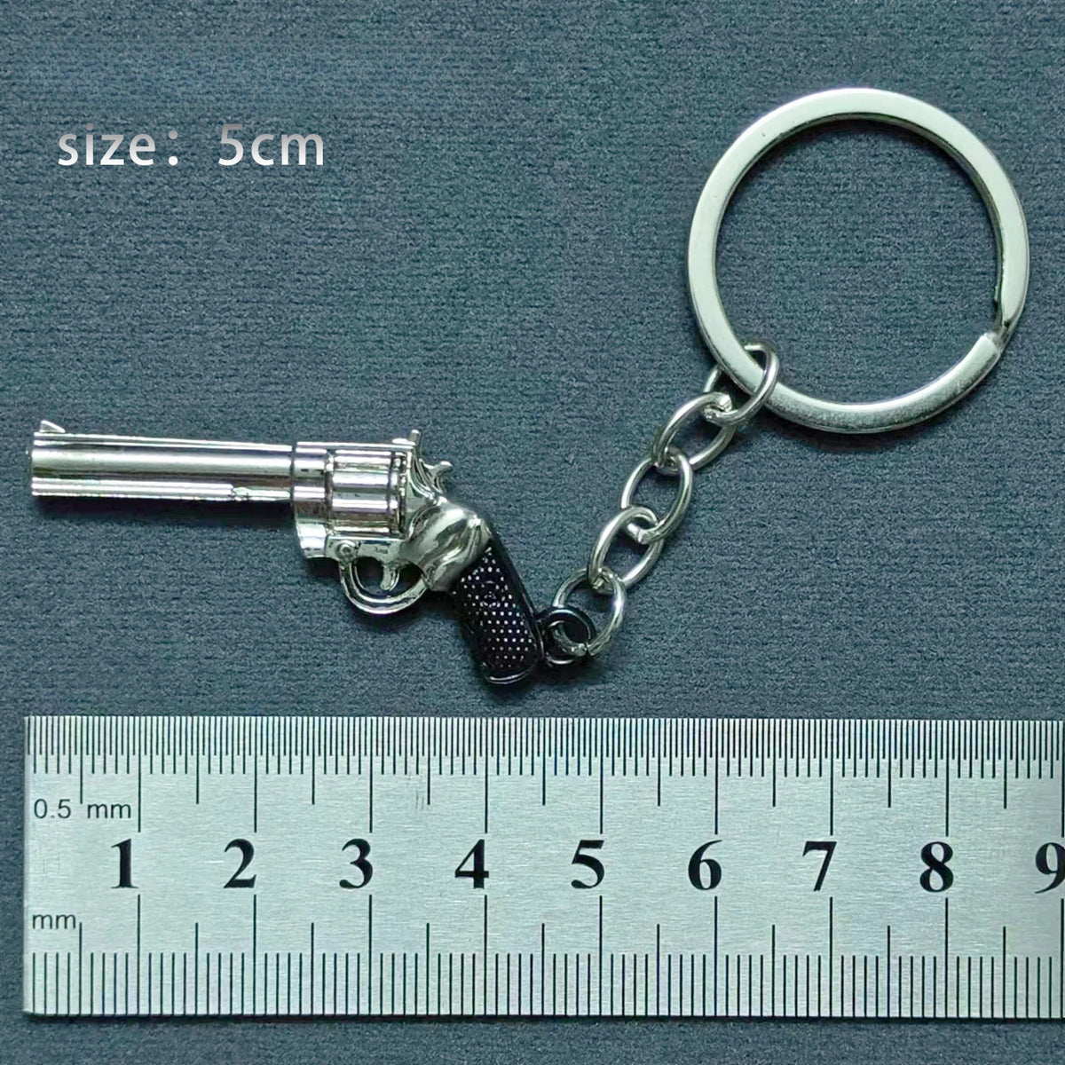 A silver alloy gun model miniature keyring with a realistic grip and barrel, shown next to a ruler.