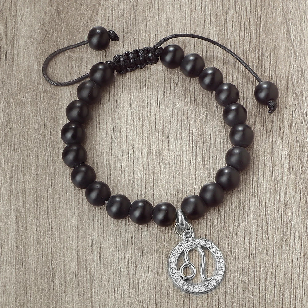 A black beaded bracelet with a silver zodiac charm is displayed on a neutral background.