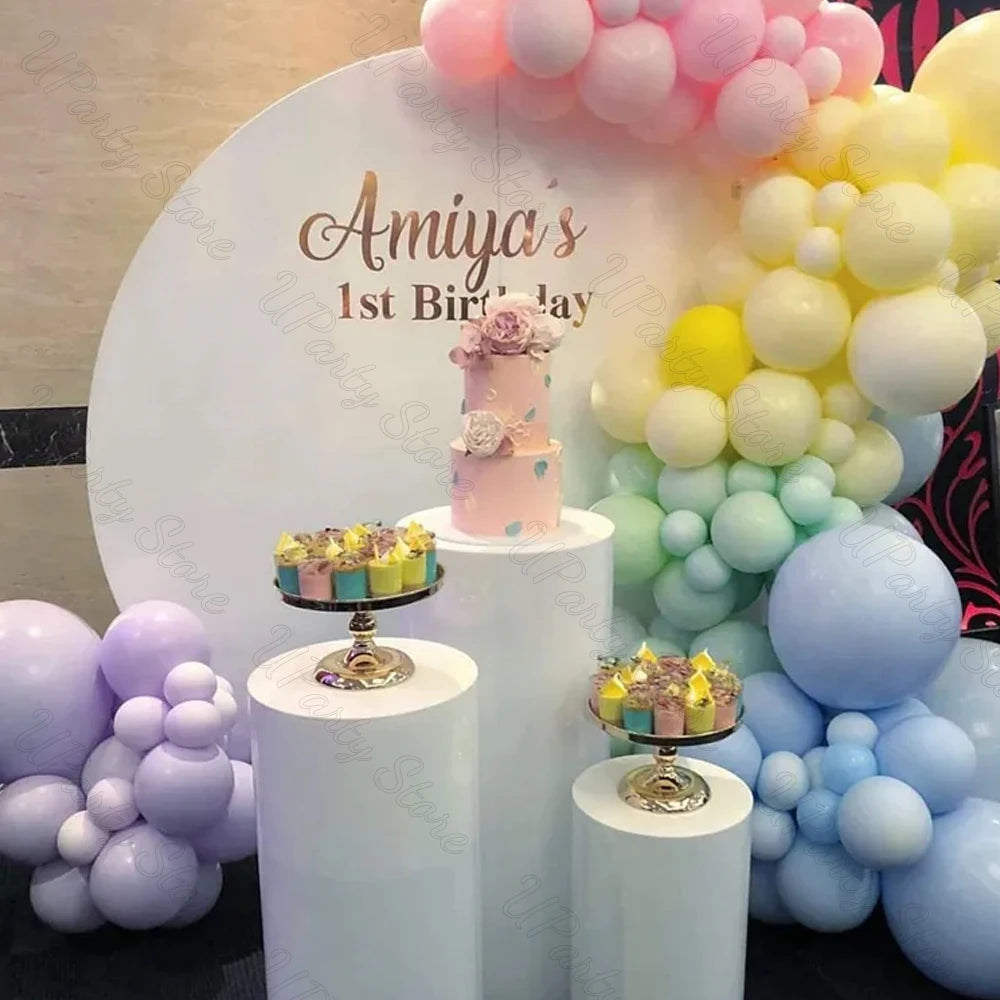 A display of pastel macaron latex balloons in pink, yellow, and blue clustered around a cake and decorative backdrop.
