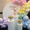 A display of pastel macaron latex balloons in pink, yellow, and blue clustered around a cake and white pillars.
