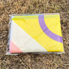 A yellow and purple pride rainbow flag banner rolled up in clear plastic on dry grass.