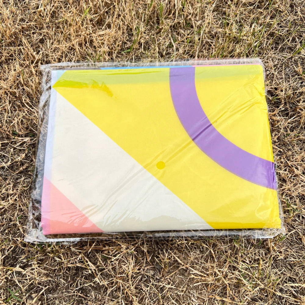 A yellow and purple pride rainbow flag banner rolled up in clear plastic on dry grass.