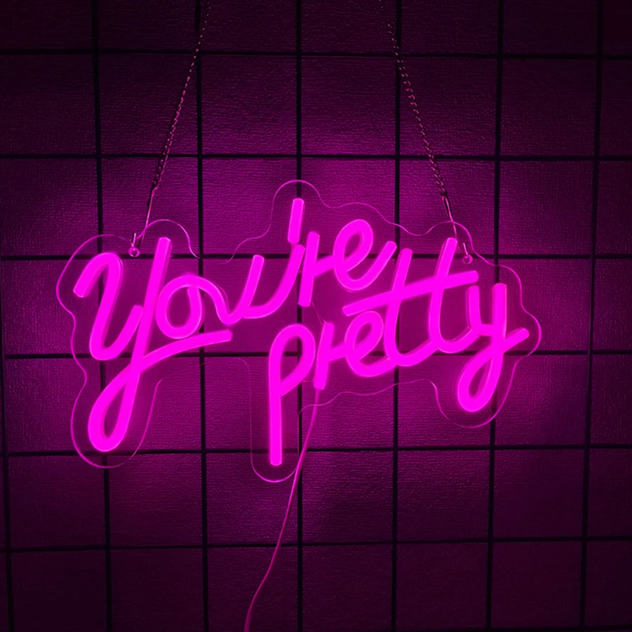 A glowing pink neon sign spelling out You're pretty against a dark purple grid background.